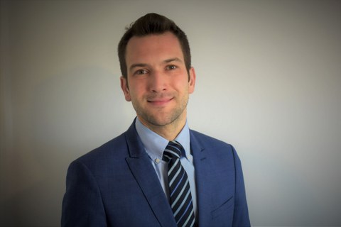 Mann mit kurzem braunen Haar und blauem Anzug lächelt in die Kamera