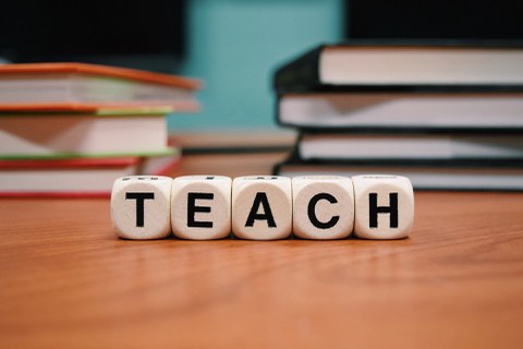 Fünf nebeneinander liegende Buchstabenwürfel bilden das Wort Teach.