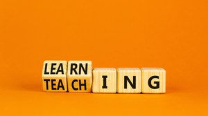 Holzwürfel vor einem orangen Hintergrund, auf denen Teaching und Learning geschrieben steht