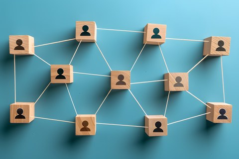 Wooden blocks with engraved person icons are connected by white strings, forming a network on a blue background. The image visualizes human networking and symbolizes collaboration and cooperation.