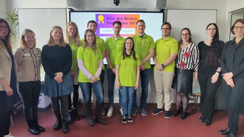 Das Bild zeigt die Preisträger:innen des besten Tutoriums 2024. Zu sehen ist eine große Gruppe von Menschen, die in einem Seminarraum steht.