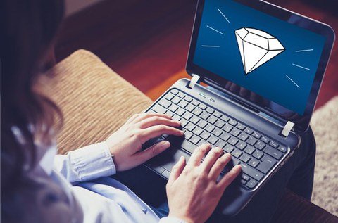 Person sitting on a couch typing on a laptop; a diamond icon is displayed on the screen.