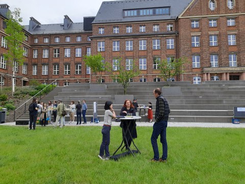 Numerous people are standing on a lawn in front of a large building and chatting.