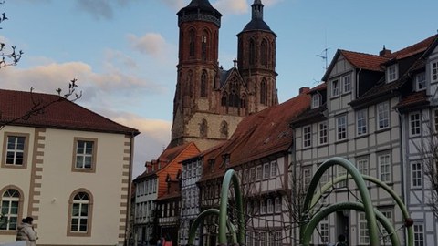 Playground in front of a historic old town setting with half-timbered houses; in the background, the twin-towered façade of the Gothic Market Church of St. Cosmas and Damian in Einbeck under a blue, partly cloudy sky.