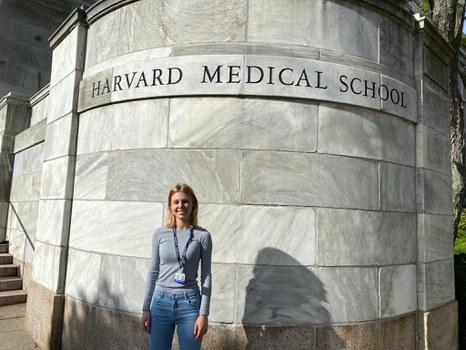 A young woman stands in front of a wall labeled Harvard Medical School.