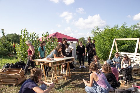 Young people sit and stand outside in a field and work.