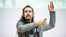 Gustavo Rosales präsentiert seinen Science Slam. Er hat seine Arme nach oben gestreckt und gestikuliert. 