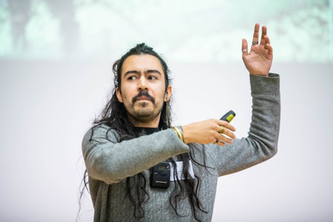 Gustavo Rosales präsentiert seinen Science Slam. Er hat seine Arme nach oben gestreckt und gestikuliert. 