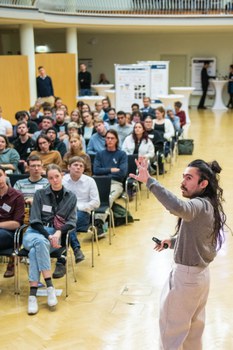 Gustavo Rosales präsentiert seinen Science Slam vor Publikum. Er deutet auf seine Präsenation