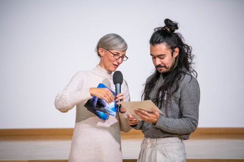 Henriette Greulich und Gustavo Rosales schauen beide auf die überreichte Urkunde