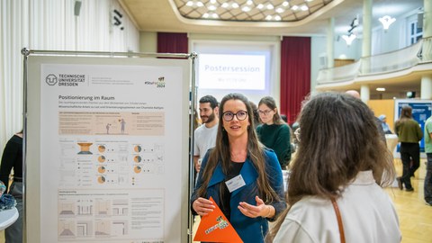 Zwei Studentinnen stehen neben einem wissenschaftlichen Poster und unterhalten sich