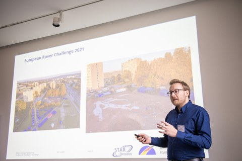 Ein Mann hält eine Präsentation. Im Hintergrund ist seine PoewrPoint an die Wand projeziert.