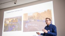 Ein Mann hält eine Präsentation. Im Hintergrund ist seine PoewrPoint an die Wand projeziert.