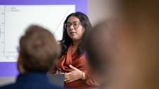Eine Studentin hält einen Vortrag. Im Vordergrund ist verschwommen das Publikum zu erkennen.