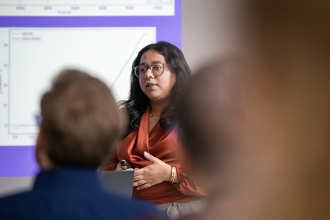 Eine Studentin hält einen Vortrag. Im Vordergrund ist verschwommen das Publikum zu erkennen.