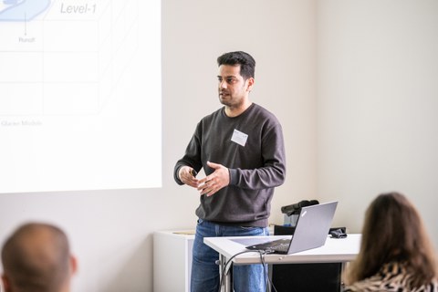 Ein Student hält eine Präsentation und steht hinter einem Pult mit seinem Laptop darauf.