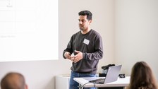 Ein Student hält eine Präsentation und steht hinter einem Pult mit seinem Laptop darauf.