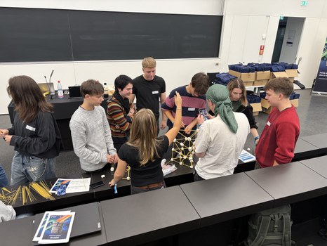Studierende arbeiten in Gruppen an einem Bauprojekt aus Spaghetti und Marshmallows in einem Hörsaal.