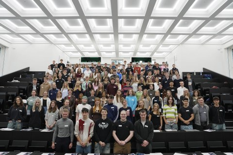 Viele Studierende stehen in einem großen Hörsaal für ein Gruppenbild zusammen.