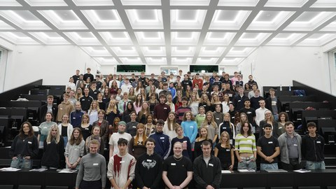 Many students are standing together in a large lecture hall for a group photo.