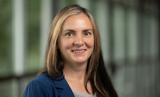 The image shows a staff member with long dark hair smiling at the camera.