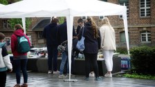 Menschen stehen im Regen vor einem Zelt.