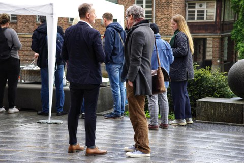 Menschen stehen im Regen vor einem Zelt.