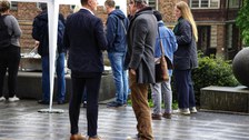 Menschen stehen im Regen vor einem Zelt.