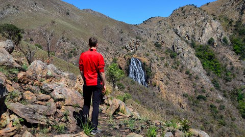Bild eines Nationalparks in Eswatini. Im Vordergrund steht eine Person, die auf einen Wasserfall im Hintergrund schaut.