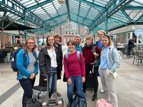 Gruppe von acht Frauen mit ihrem Gepäck. Im Hintergrund ist die Überdachung des Bahnhofsgebäudes zu sehen.