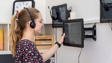 Junge Frau nutzt Wandbildschirm und hat Kopfhörer dabei auf
