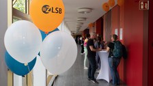 Foto eines Ganges mit Menschen, im Vordergrund Luftballons zum ZLSB Jubiläum.