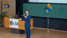 Mann hält Vortrag auf einer Bühne im Hörsaal