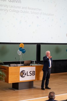 Mann steht auf Bühne eines Hörsaals und gibt Vortrag