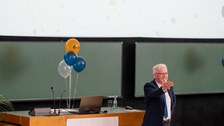 Mann steht auf Bühne eines Hörsaals und gibt Vortrag