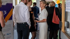 Zwei Frauen und ein Mann unterhalten sich, während im Hintergrund buntes Treiben herrscht.