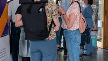 Drei Frauen unterhalten sich, während im Hintergrund buntes Treiben herrscht.
