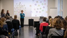 Foto zeigt einen Saal mit einer Frau, die einen Vortrag hält.