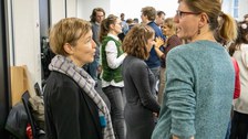 Zwei Frauen, die sich unterhalten. Im Hintergrund herrscht buntes Treiben.