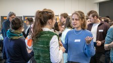 Zwei Frauen, die sich unterhalten. Im Hintergrund herrscht buntes Treiben.
