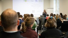 Foto zeigt einen Saal mit einer Frau, die einen Vortrag hält.