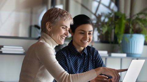 Zwei Frauen sitzen vor einem Laptop. Eine der Protagonistinnen zeigt etwas auf dem Bildschirm.