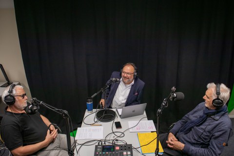 Drei Männer, die an einem Tisch sitzen und einen Podcast aufnehmen.