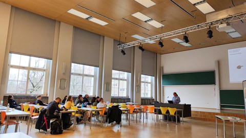 Hörsaal mir vortragender Frau am Rednerpult