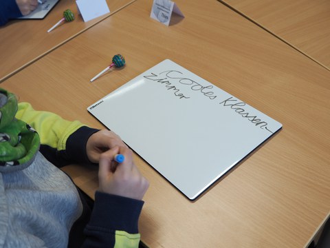 Eine Mini Whiteboard auf einem Tisch auf dem "cooles Klassenzimmer" in Schreibschrift geschrieben steht