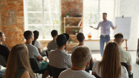 Männlicher Redner bei einem Vortrag in einem Universitäts-Workshop. Zuhörerschaft oder Konferenzsaal. Rückansicht von unerkannten Teilnehmern im Publikum.