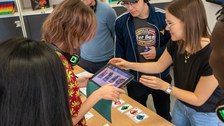 Eine Frau zeigt einer Gruppe junger Leute etwas an einem Tablet. 