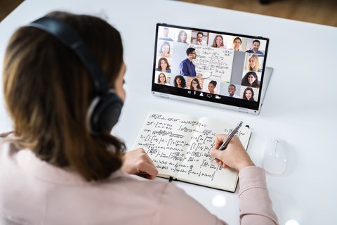 Das Foto zeigt eine Person, die Notizen in ein Heft schreibt, während sie auf ein Tablet schaut. 