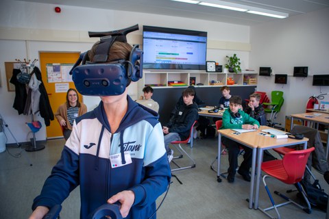 Junge mir VR-Brille. Im Hintergrund weitere Jungs in einem Klassenzimmer zu sehen.