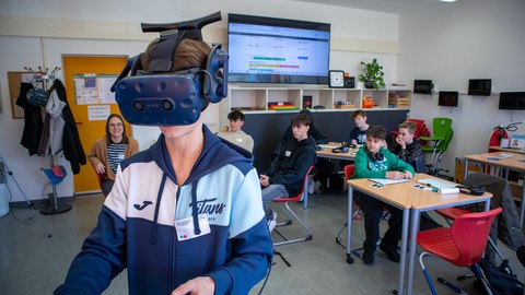 Junge mir VR-Brille. Im Hintergrund weitere Jungs in einem Klassenzimmer zu sehen.